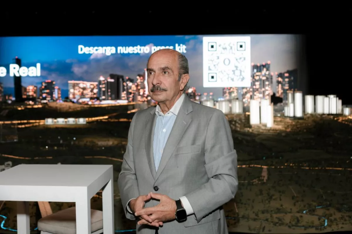 Hombre con saco gris y una imagen de una ciudad de fondo.