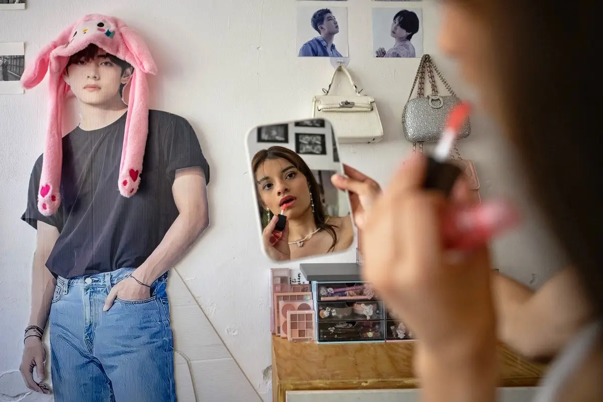 Ana Campos Rodríguez, una fan mexicana del grupo surcoreano de K-pop BTS, se maquilla junto a un recorte de cartón de la cantante de BTS Kim Tae-hyung, también conocida como V, en su casa de la Ciudad de México el 29 de abril de 2026.