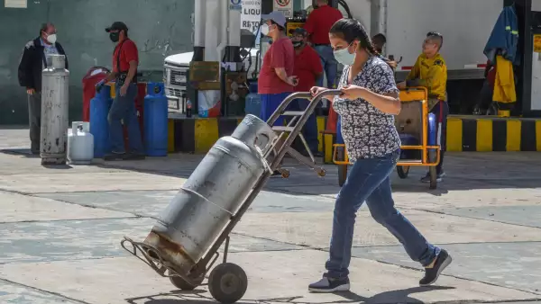 Una mujer lleva su tanque de gas LP, cuyo precio promedio subió un 25% anual