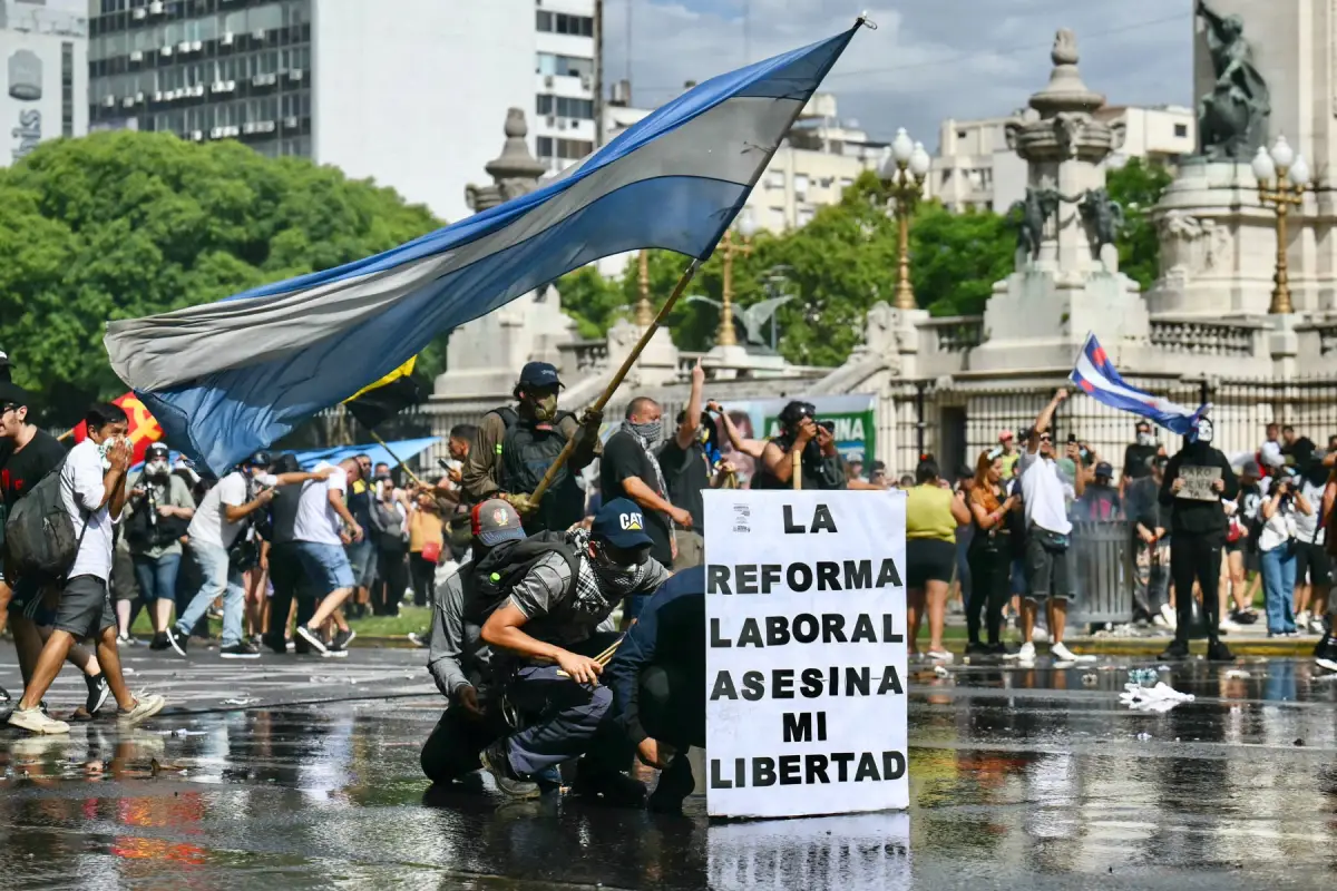 Los manifestantes se protegen detrás de una pancarta que dice "La reforma laboral mata mi libertad" de un cañón de agua disparado por la policía antidisturbios durante una protesta convocada por los sindicalistas contra el debate sobre la reforma laboral que tiene lugar en el Congreso Nacional en Buenos Aires el 11 de febrero de 2026.