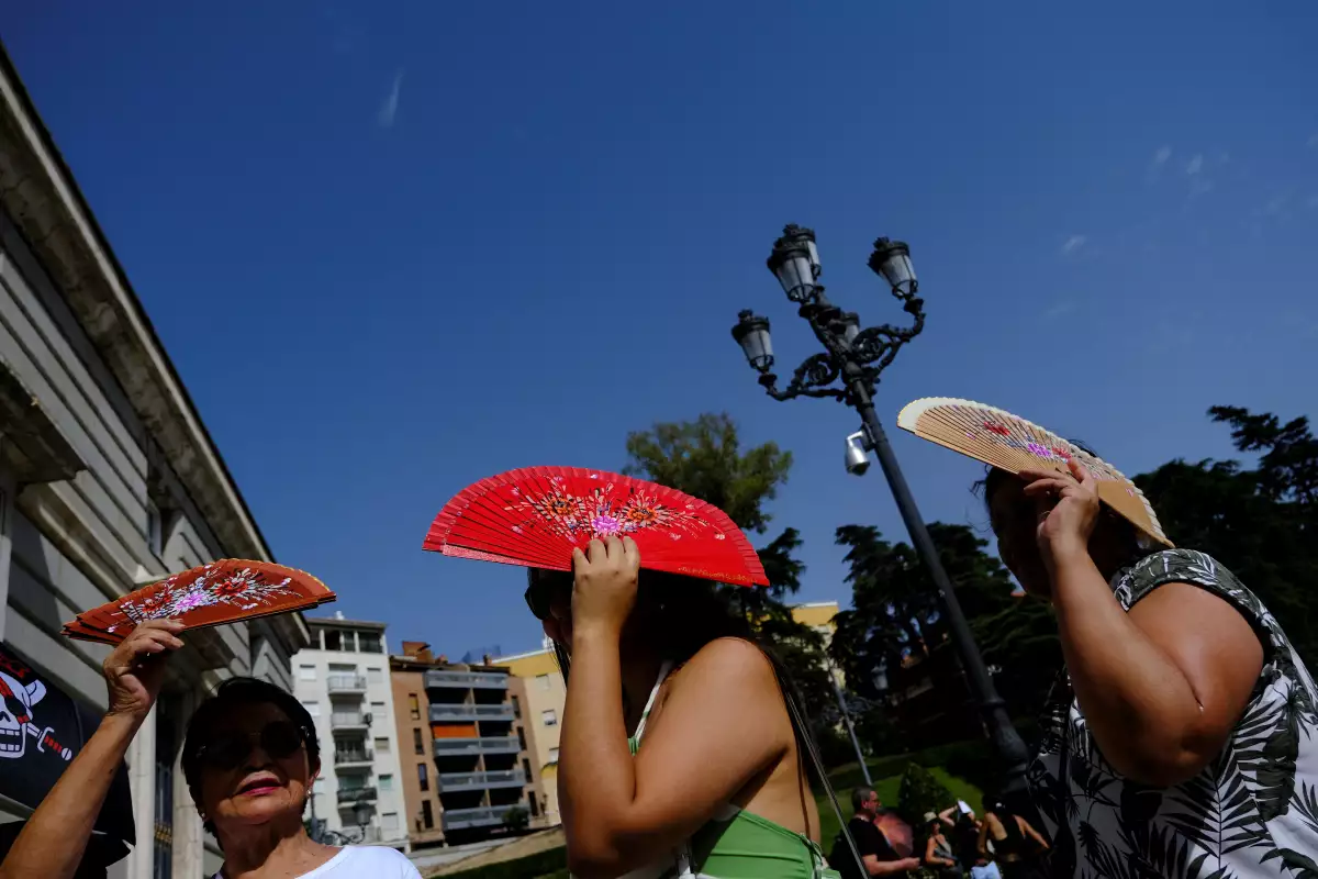 Los ciudadanos peruanos Sadith Ushinagui, de 74 años, Alisson Carrillo, de 29 años, y Carol Ore, de 50, se protegen del sol con los aficionados mientras esperan entrar en el Palacio Real durante la tercera ola de calor del verano en Madrid, España, el 8 de agosto de 2023. REUTERS/Susana Vera