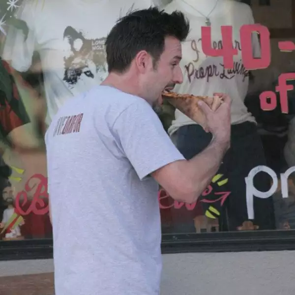 David Arquette no tiene reparo en caminar mientras se come gustosamente un enorme pedazo de pizza.
