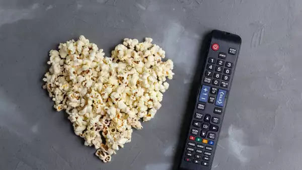 Popcorn in the shape of a heart and TV remote on grey stone background