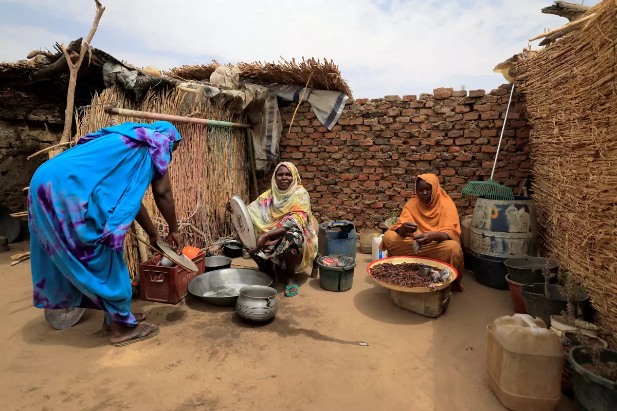 Fanna Hamit, de 58 años, una viuda chadiana que alberga en su complejo a una familia de 11 sudaneses que huyó de la violencia en la región de Darfur de Sudán, lava los platos mientras Saboura Ahmed, de 30 años, uno de sus invitados refugiados sudaneses, empaqueta grillos grandes para vender como bocadillos, en el patio de su casa
