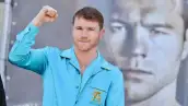 Saúl "Canelo" Álvarez vestido con una camisa azul claro, sonriente y con un puño arriba, en una foto de plano medio corto. 