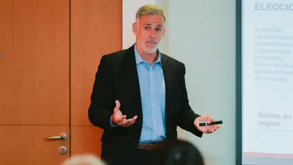 Claudio Beramendi, director general de Adium en Argentina. Viste una camisa azul cielo con un saco azul marino. Tiene las manos extendidas y en la izquierda sostiene un control remoto. 