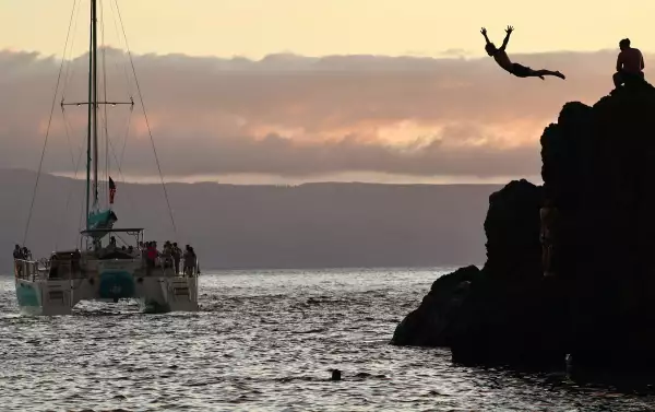 Una persona se sumerge en las rocas mientras un barco turístico pasa por la playa de Kaanapali, un destino turístico popular, el 5 de agosto de 2024 cerca de Lahaina, Hawái. En junio, Maui vio una disminución del 22 por ciento en las llegadas de visitantes y una disminución del 27 por ciento en el gasto de los visitantes en comparación con 2023, según el Departamento estatal de Negocios, Desarrollo Económico y Turismo. El 8 de agosto marca el primer aniversario de los incendios forestales de Maui que mataron a 102 personas y devastaron la histórica comunidad de Lahaina en el oeste de Maui.