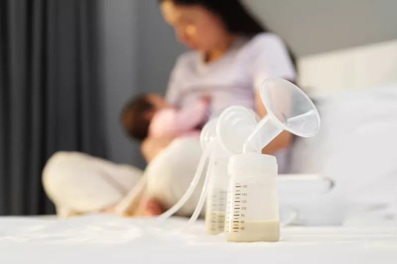 the breast milk are in the bottles of electric breast pumping set on bed with mother breastfeeding newborm baby background