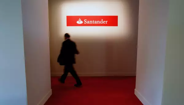 (Un hombre camina frente a un letrero de banco Santander)