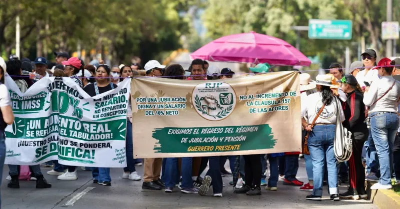 Dos carteles, uno blanco y uno café con verde que portan personas en una avenida con árboles y sombrillas.jpg
