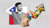 Un hombre vestido con una camiseta de rayas se rasca la cabeza, con una bolsa de la compra con los productos subiendo en forma de flecha ascendente en frente y una bandera de Chile de fondo. 