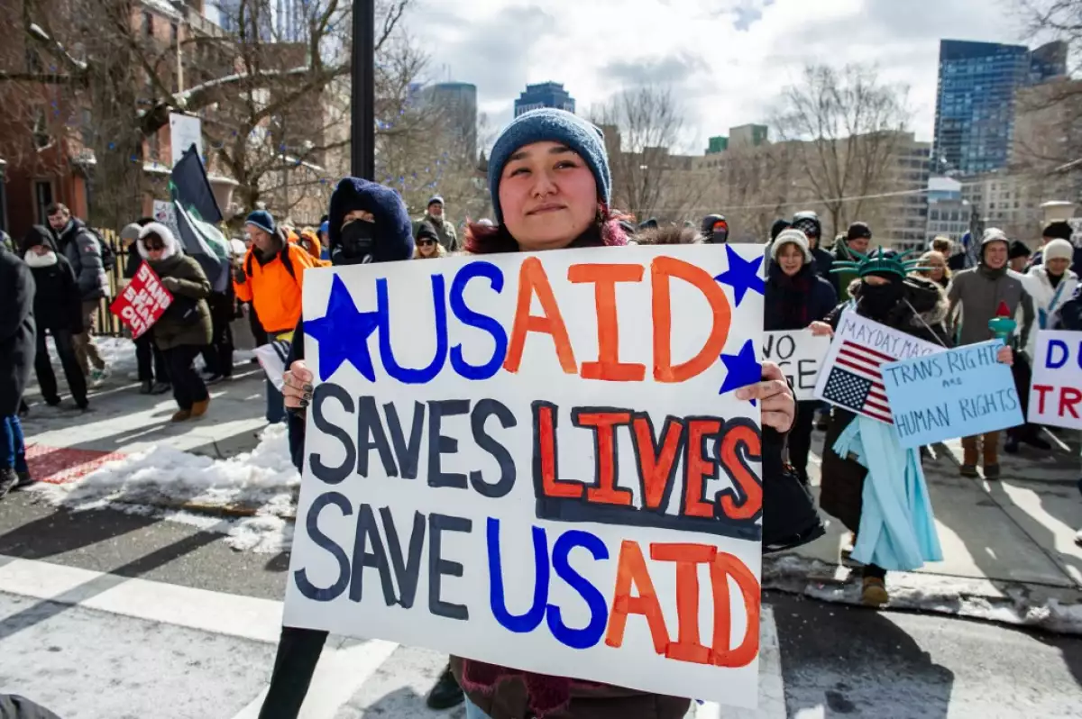 Una mujer sostiene un cartel que apoya a USAID mientras los manifestantes se manifiestan contra el presidente estadounidense Donald Trump y sus políticas durante una protesta cerca de la Casa Estatal de Massachusetts en el Día del Presidente el 17 de febrero de 2025, en Boston, Massachusetts.