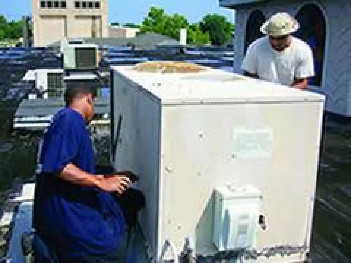 Dos trabajadores reinstalan una unidad de 5 toneladas despu�s de repararla. El mantenimiento preventivo de las unidades de aire acondicionado pudo evitar este gasto innecesario.