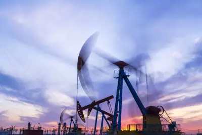 Sitio del campo petrolero, por la noche, las bombas de aceite están funcionando, la bomba de aceite y la hermosa puesta de sol reflejadas en el agua, la silueta de la unidad de bombeo de vigas por la noche.