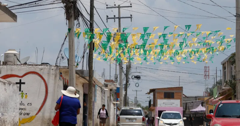 Una calle en donde se observan cables de luz, una camioneta, un coche blanco y uno rojo