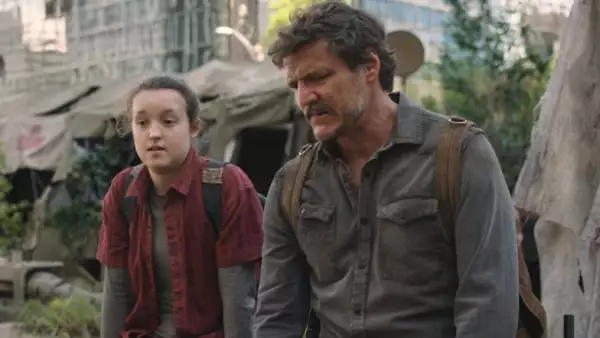 Foto de una escena de The Last Of Us con Ellie (Bella Ramsey) y Joel (Pedro Pascal) sentados lado a lado con una ciudad en ruinas detrás de ambas.