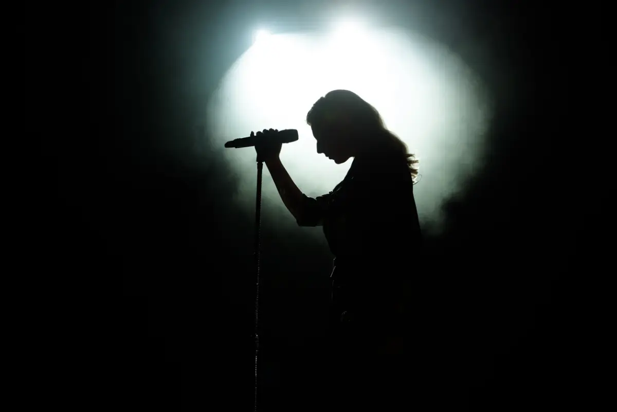 Silueta negra de una mujer cantante sobre un reflector blanco. 