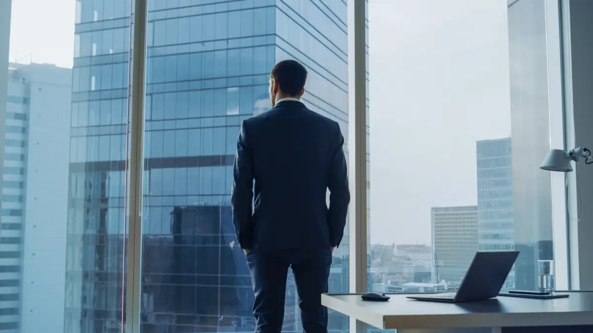 Director de una empresa viendo desde su ventana hacia otros edificios de la ciudad.