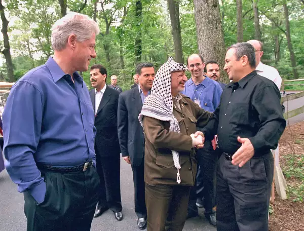 El presidente estadounidense Bill Clinton observa mientras el líder palestino Yasser Arafat y el primer ministro israelí Ehud Barak se dan la mano en el día de apertura de las conversaciones de paz en Oriente Medio el 11 de julio de 2000 en Camp David MD. 