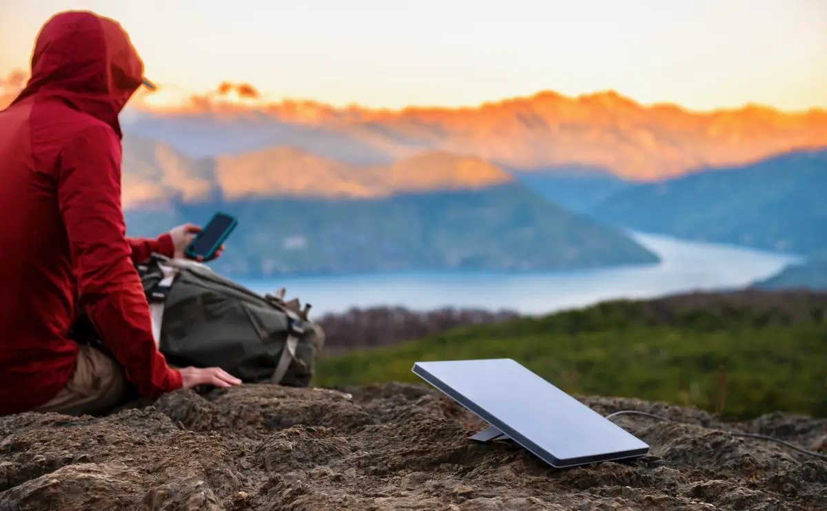 Una persona en medio de una montaña buscando internet con una antena de Starlink.