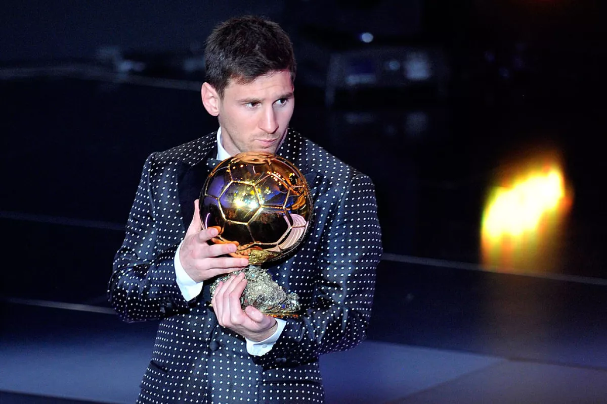 Foto de Lionel Messi con un traje negro y lunares blancos, con el balón de oro entre sus manos.