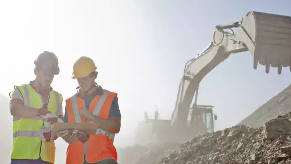 dos trabajadores de la construcción parados en una obra con escombros y maquinaria