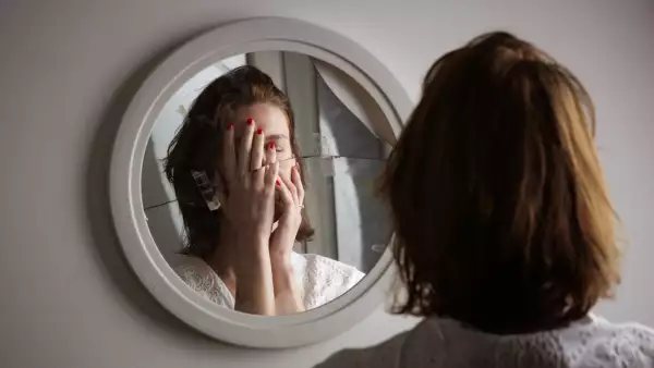 El trastorno bipolar tiene varios síntomas. (Mujer frente a un espejo tapándose la cara)