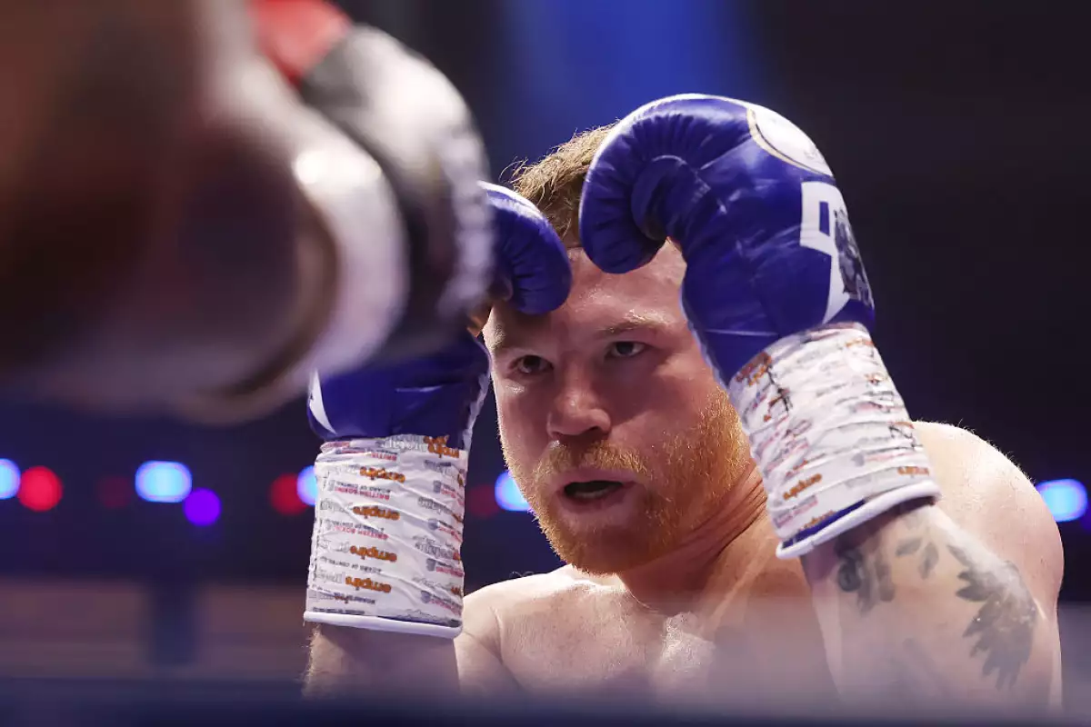 Foto del canelo alvarez levantando los puños con guantes azules de la marca amiri en la pelea contra william scull en riad, arabia saudita.