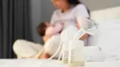 the breast milk are in the bottles of electric breast pumping set on bed with mother breastfeeding newborm baby background