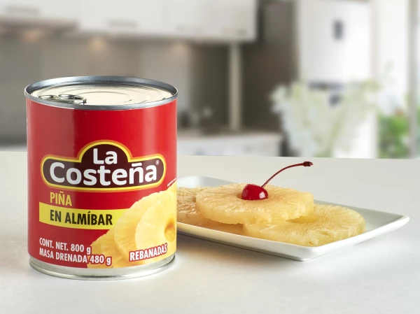 Lata de piña en almibar de La Costeña con piñas en un plato atrás