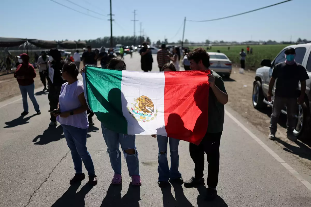 La gente sostiene una bandera mexicana mientras los agentes federales de los Estados Unidos (que no se muestran en la foto) bloquean un camino que conduce a una instalación agrícola donde los agentes federales de los Estados Unidos y los oficiales de inmigración realizaron una operación, en Camarillo, California, EE. UU., el 10 de julio de 2025.