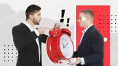 Dos hombres de traje frente a frente con un reloj en las manos. 