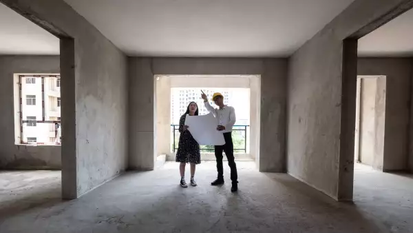 Dos personas viendo planos en una vivienda en obra gris