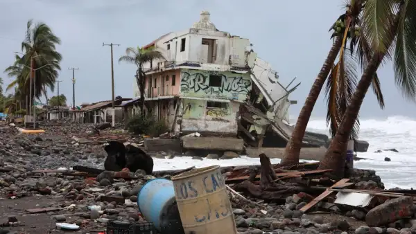 En la imagen se observa una vivienda destruida por el paso del huracán Simón en Colima, así como palmeras dañadas y basura arrastrada a la orilla del mar.