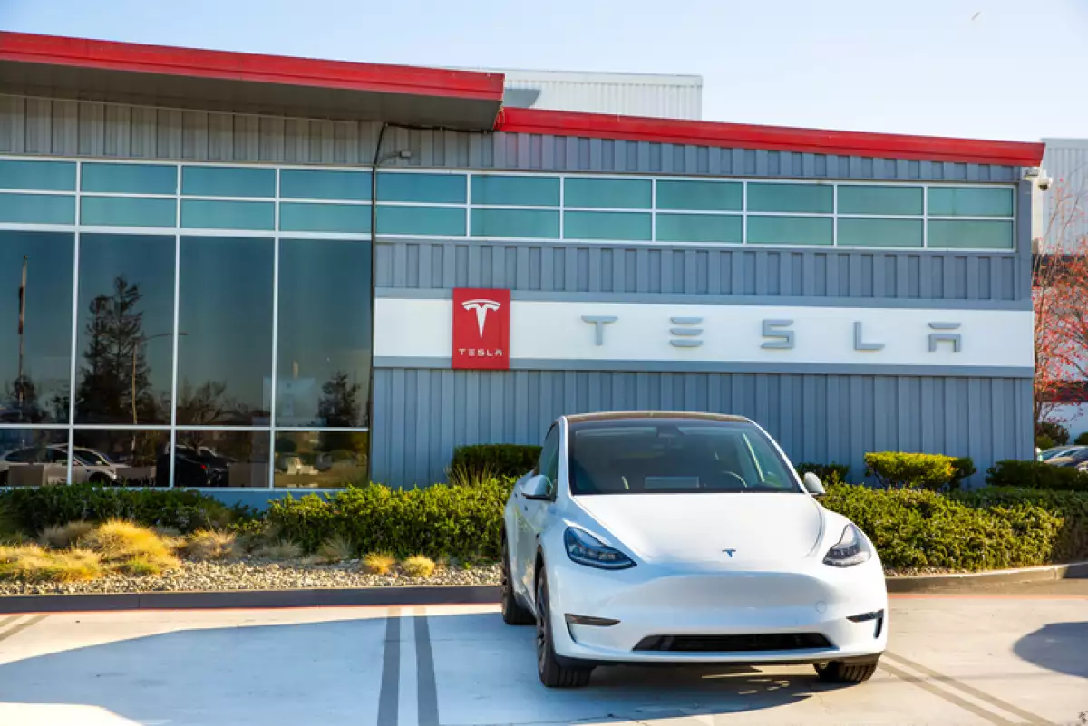 Auto blanco de Tesla estacionado frente a un almacen de Tesla.