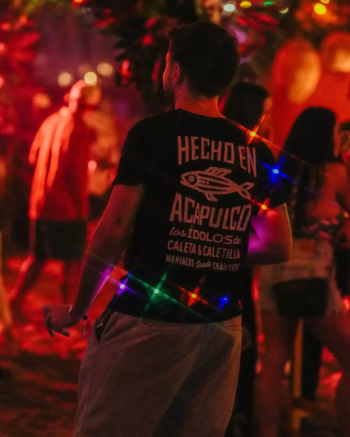 joven de espalda con una playera que dice "Hecho en acapulco" en un fondo iluminado de rojo.