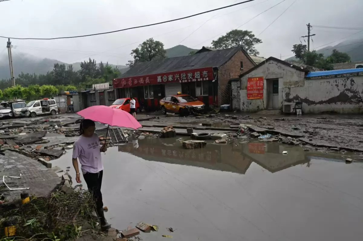 Una mujer camina por una carretera dañada después de las fuertes lluvias en el distrito de Fangshan en Beijing el 1 de agosto de 2023. Al menos 11 personas murieron y 13 desaparecieron después de que las fuertes lluvias azotaron Beijing, dijeron los medios de comunicación estatales el 1 de agosto, en aguaceros que han sumergido las carreteras y han inundado los vecindarios con barro