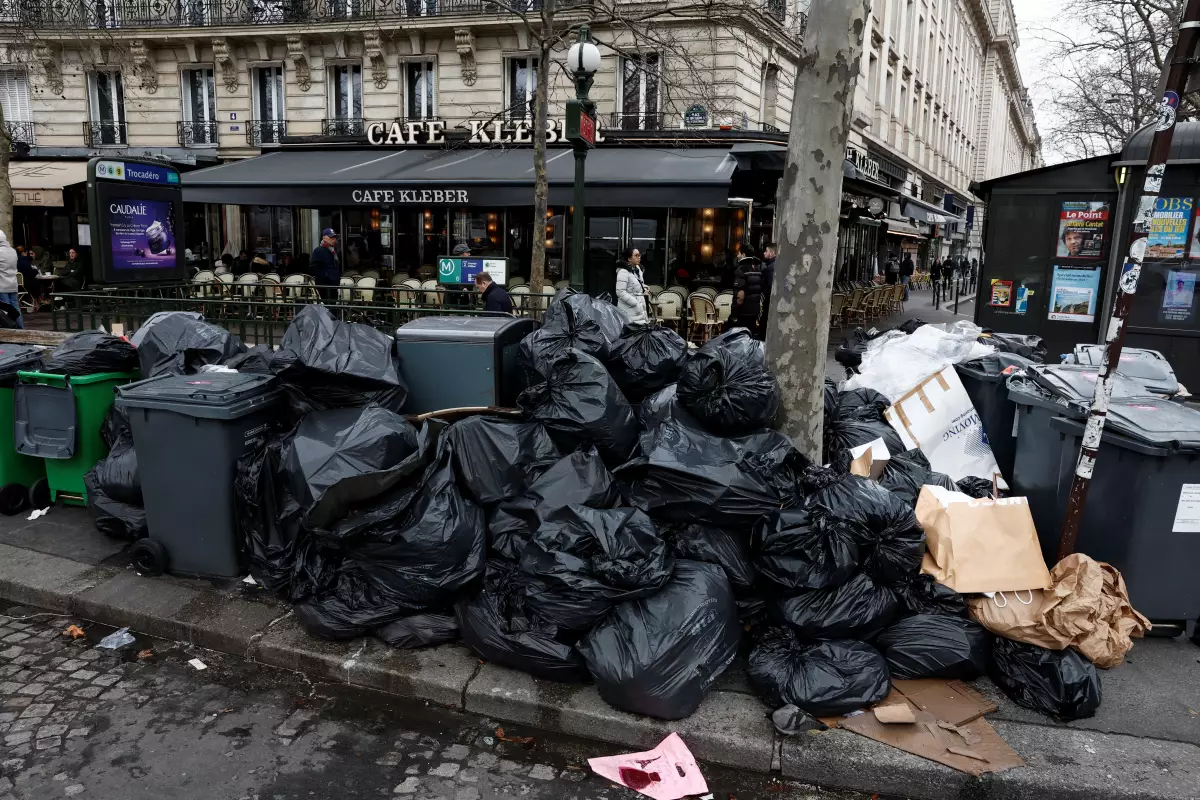 Gente camina en la calle donde los botes de basura están rebasados y la basura no ha sido recolectadas