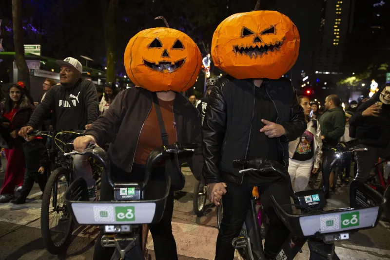 ciclistas con cascos de calabaza participan en el paseo nocturno de dia de muertos