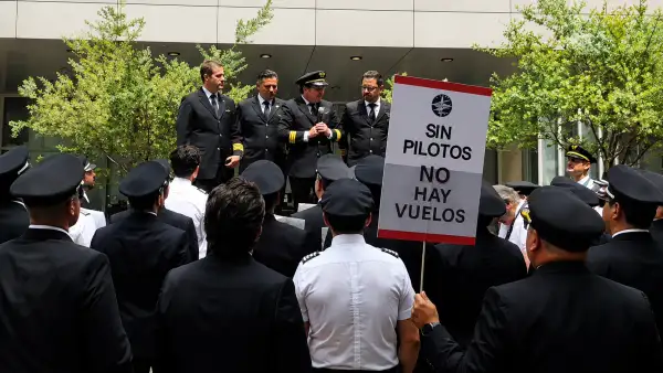 Espaldas de hombres con trajes  y gorras de capitanes. Un letrero que dice: sin pilotos no hay vuelos.jpg