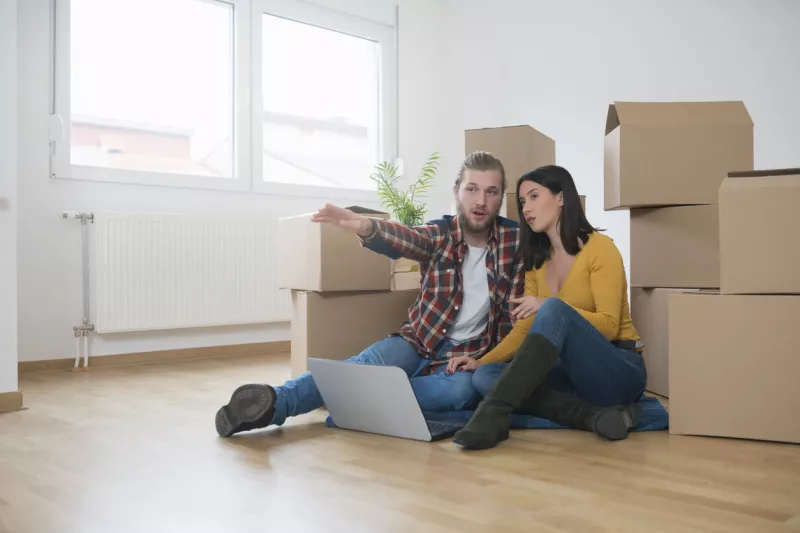 Joven pareja heterosexual sentada en el suelo entre cajas de cartón y planeando cómo organizar el interior de su nuevo apartamento.