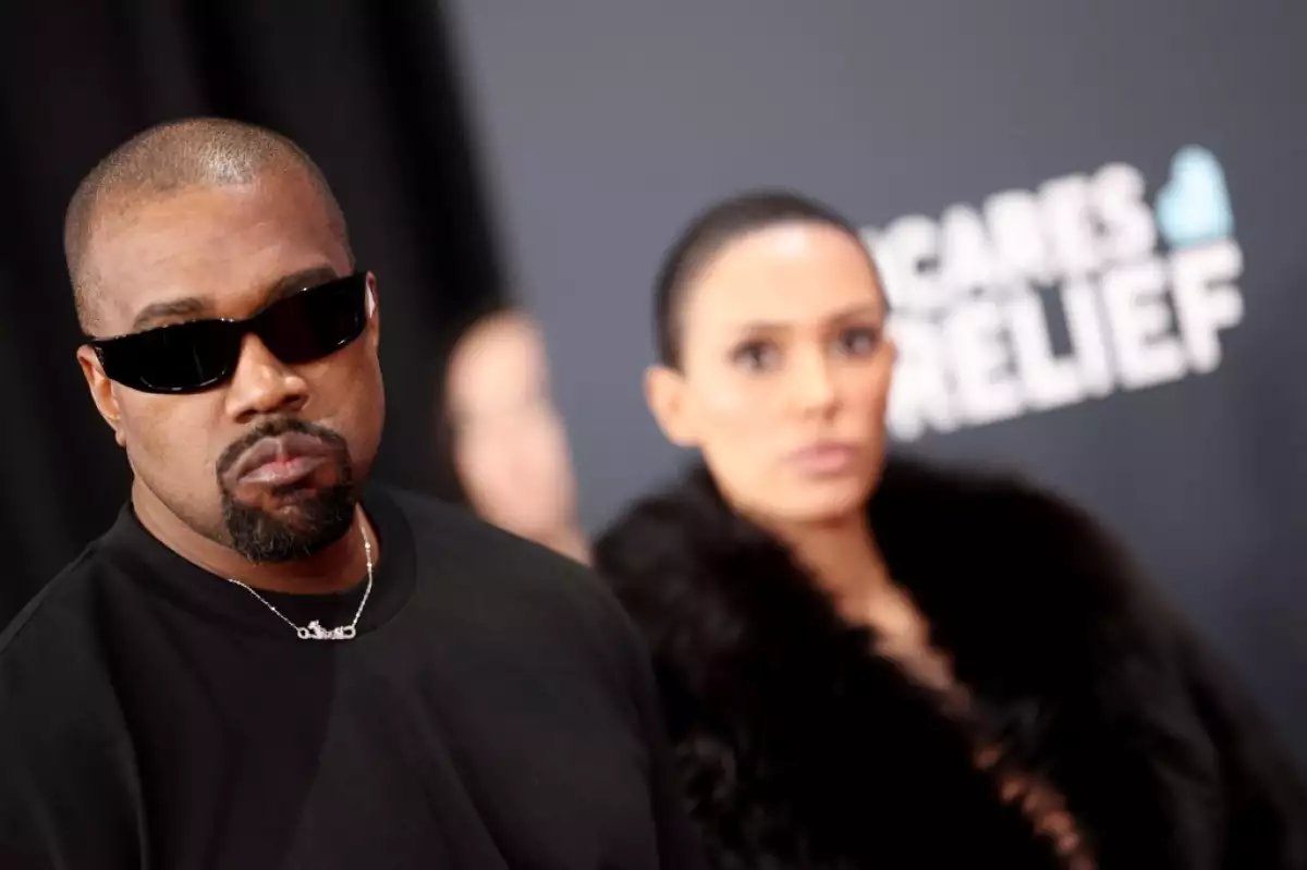 Foto de Kanye West vestido de negro con lentes oscuros y detrás de él la arquitecta Bianca Censori, con quien está casado desde hace cuatro años.