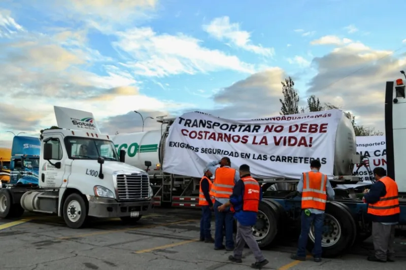 Transportistas frente a sus camiones durante el paro nacional de este 26 de octubre. En uno de los camiones cuelga una manta que dice "Transportar no debe costarnos la vida". 