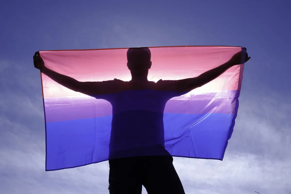 adult man on his back with bisexual flag on a sunny day.