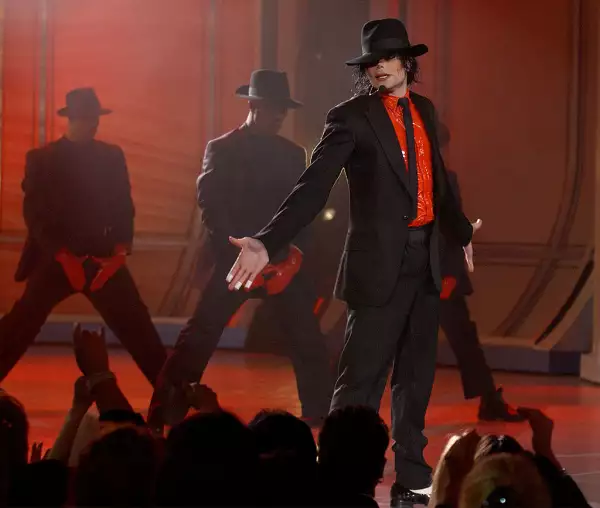 Foto de Michael Jackson en un concierto especial en 2002 vestido de camisa roja y traje, corbata y sombrero en color negro.