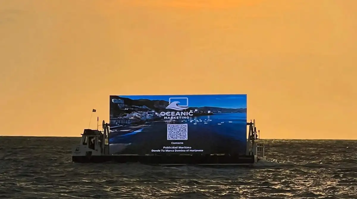 Atardecer, en el mar se observa una embarcación con una pantalla led que promociona a la empresa Oceanic Marketing.