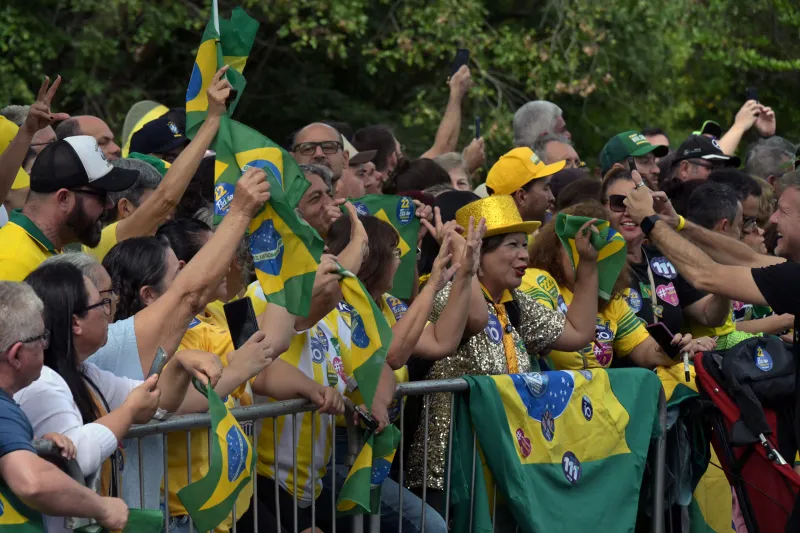 Personas con banderas de Brasil tras una valla en espera de que pasen los candidatos a la presidencia de Brasil.
