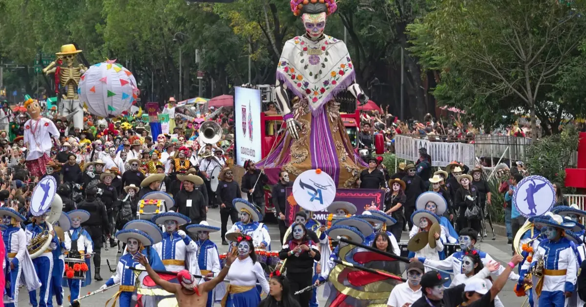 Dos catrinas gigantes con huipiles. Hombres y mujeres vestidos de blanco y azul con maquillaje de catrinas.jpg