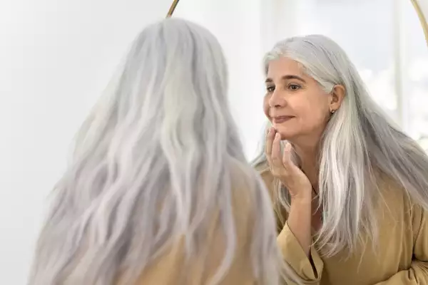 Positive,Focused,Elderly,Latin,Woman,Looking,In,Mirror,,Touching,Chin,
