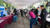 Un pasillo largo al aire libre con mesas al lado y mujeres y hombres hablando, traen folletos en la mano .jpg